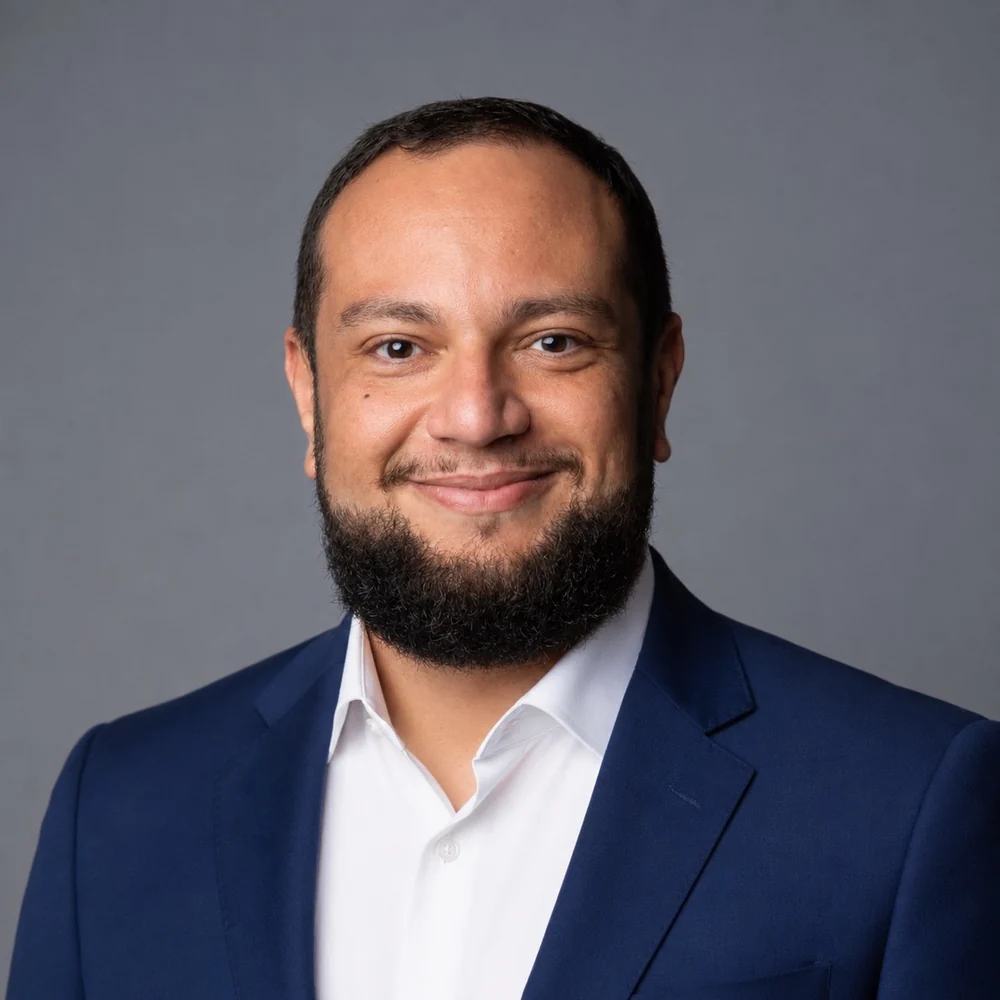Retrato de Nilson Gonçalves, de blazer azul e camisa branca, diante de um fundo cinza.